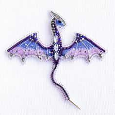 a purple and blue dragon brooch sitting on top of a piece of cloth next to a needle