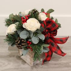 a christmas arrangement with white roses and greenery in a wooden box on a table