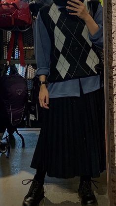 a woman standing in front of a mirror wearing a black and white argyle sweater over a pleated skirt