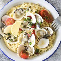 a white bowl filled with pasta and clams on top of a gray tablecloth