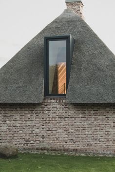 a brick building with a thatched roof and window on the side, in front of a grassy area