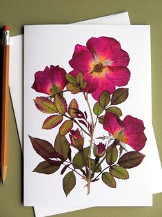 some pink flowers are next to a pencil on a green surface with a white card