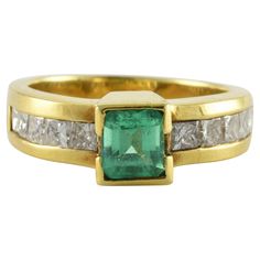 A vibrant green emerald-shaped Colombian emerald measuring approximately 0.50 carats is the centerpiece of this estate band set in a substantial 18kt yellow gold mounting, accented on the shoulders with ten princess cut diamonds, in a channel setting totaling approximately 1.00 carats, F color, SI clarity. Gold Emerald Ring With Channel Set Emerald Cut, Green Emerald-cut Channel Set Jewelry, Gia Certified Green Princess Cut Diamond Ring, Gia Certified Green Princess Cut Rings, Fine Jewelry Green Channel Set Ring, Formal Fine Jewelry Emerald Ring Channel Set, Emerald Channel Set Jewelry With Emerald Cut, Green Diamond Channel Set Rings, Yellow Gold Emerald Cut Emerald Ring With Channel Set