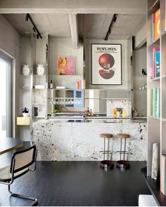 a kitchen with two stools in front of the counter and bookshelves on the wall