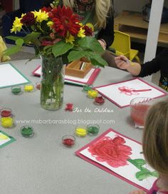 a woman sitting at a table with two children and flowers in a vase on the table