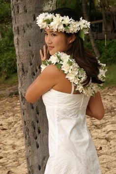 a woman in a white dress standing next to a tree with flowers on her head