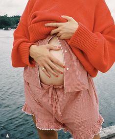 a woman in red sweater and shorts holding her stomach by the water's edge