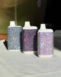 three different colored bottles sitting on top of a white tablecloth covered table next to a window