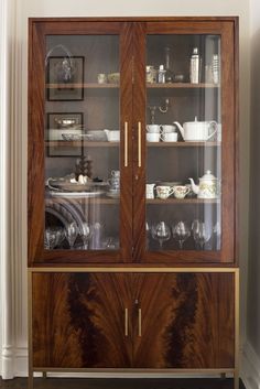 a wooden cabinet with glass doors and dishes on it's shelves in front of a white wall