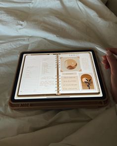 a person is holding an open notebook on top of a bed