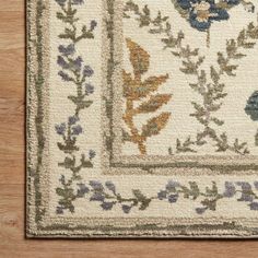 an area rug with blue flowers and green leaves on the border, in front of a wooden