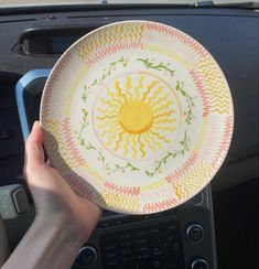 a person is holding up a plate in their car's dash board area, with the sun painted on it