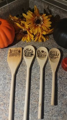 four wooden spoons sitting on top of a counter next to a pumpkin and sunflower