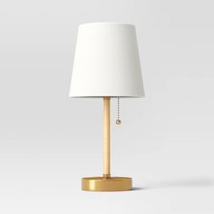 a white lamp with a gold base and a white lampshade on the side