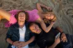 three people laying in the sand with one person holding a cell phone