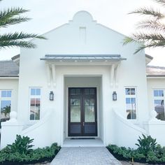 a white house with palm trees in front of it and the door is open to let in light