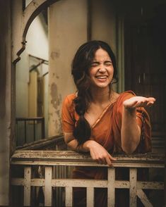 a woman in an orange dress is smiling and holding her hand out to the side