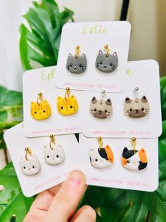 the cat earrings are on display in front of some green plants and a white card