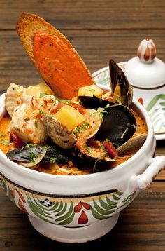 a bowl filled with clams, bread and sauce on top of a wooden table