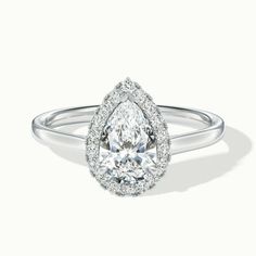 a pear shaped diamond ring with diamonds on the band and an oval halo setting in white gold