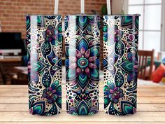 three colorful floral designs on the side of two travel mugs sitting on top of a wooden table