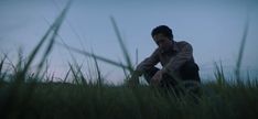 a man sitting in tall grass with his hand on his face and looking at the ground