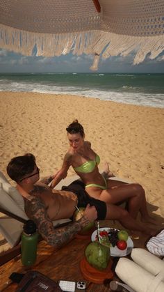 a man and woman sitting on top of a beach next to each other near the ocean