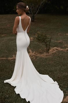 a woman in a white wedding dress standing on the grass with her back to the camera