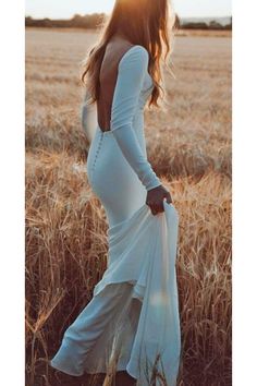 a woman in a white dress is standing in a wheat field with her back to the camera