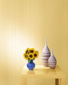 two vases with sunflowers sit on a small table in front of a yellow wall