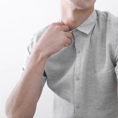 a young man is adjusting his collar in front of the camera while wearing a gray shirt