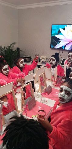 several people with face paint sitting at a table in front of a tv and holding up their hands