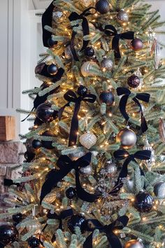 a decorated christmas tree with black and silver ornaments on the top, ribboned around it