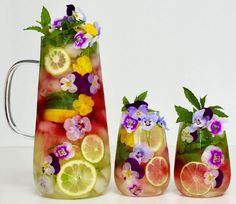 three pitchers filled with fruit and flowers next to each other