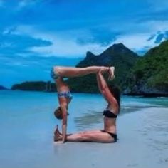 two women in bikinis doing yoga on the beach