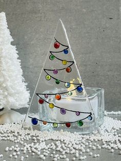 a small glass christmas tree sitting on top of a table next to a white candle