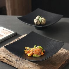 two black plates topped with food on top of a wooden table