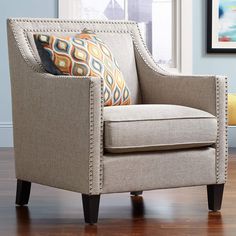 a living room chair with pillows on top of it in front of a window and wooden floor