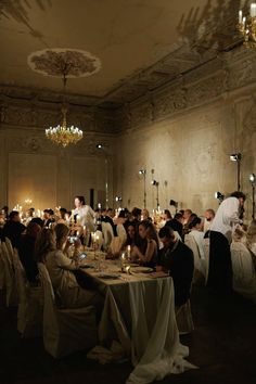 a group of people sitting around a table in a room with chandeliers on the ceiling