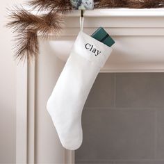 a white christmas stocking hanging from a mantel with the word clay on it