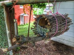 a bird feeder made out of branches and logs hanging from a chain on a fence