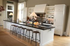 a kitchen with white cabinets and black counter tops, an island in the middle is surrounded by four stools