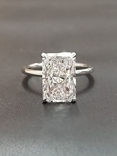 a princess cut diamond engagement ring on a gray surface with the center stone in white gold