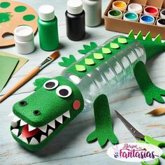 a green plastic alligator sitting on top of a wooden table next to paint and supplies