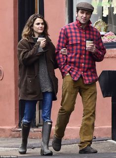 a man and woman walking down the street holding coffee in their hands while looking at each other