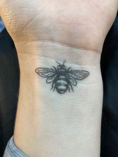 a small black and white bee tattoo on the wrist