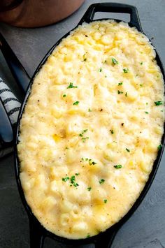 an oval casserole dish with cheese and parsley on top, next to a spoon