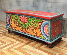 an ornately painted chest sitting on top of a hard wood floor next to a brick wall