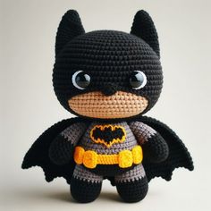 a crocheted batman doll is posed on a white surface with eyes wide open