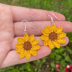 a pair of yellow crocheted sunflower earrings on a person's hand